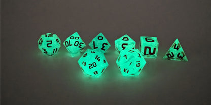 A straight on photo of a standard set of DnD dice that have black swirls showing through glow-in-the-dark green and orange numbers focusing on 2 d20s in the center. The d20 on the left has the 20 face centered and the d20 on the right has the 1 face centered. The other 6 dice are lined up in the background.