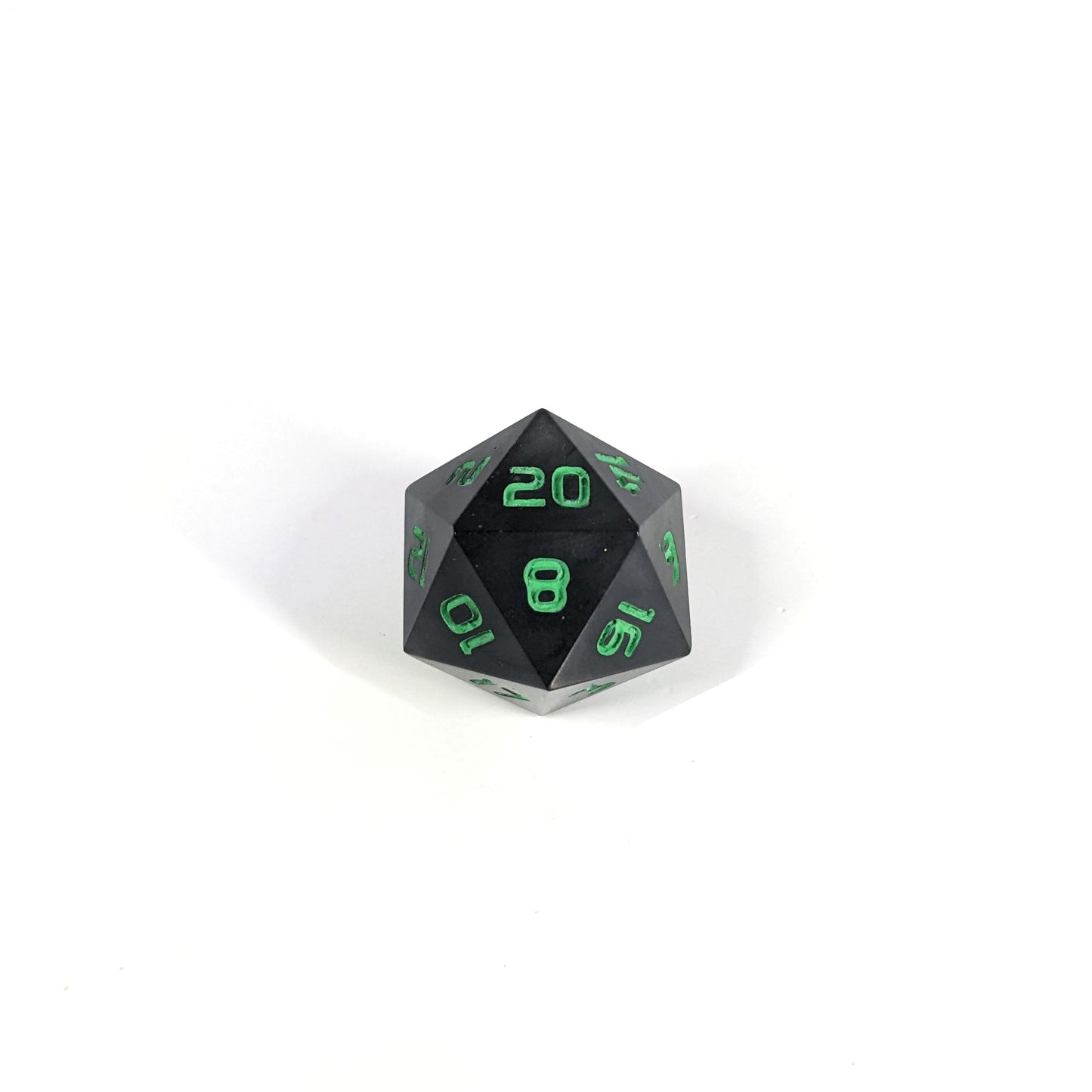A high angle photo of a standard d20 with black swirls and green numbers with the 20 face up on a white background.