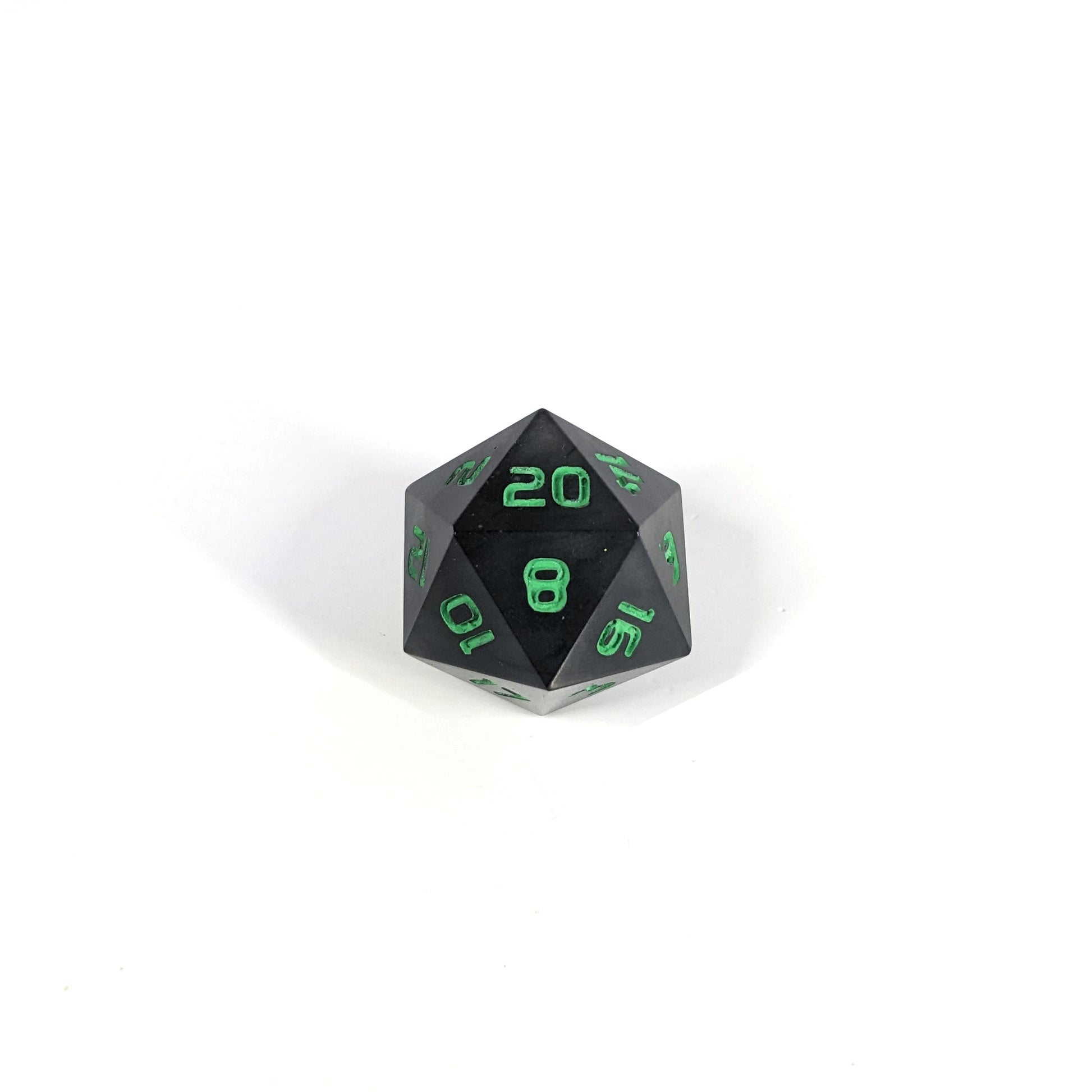 A high angle photo of a standard d20 with black swirls and green numbers with the 20 face up on a white background.