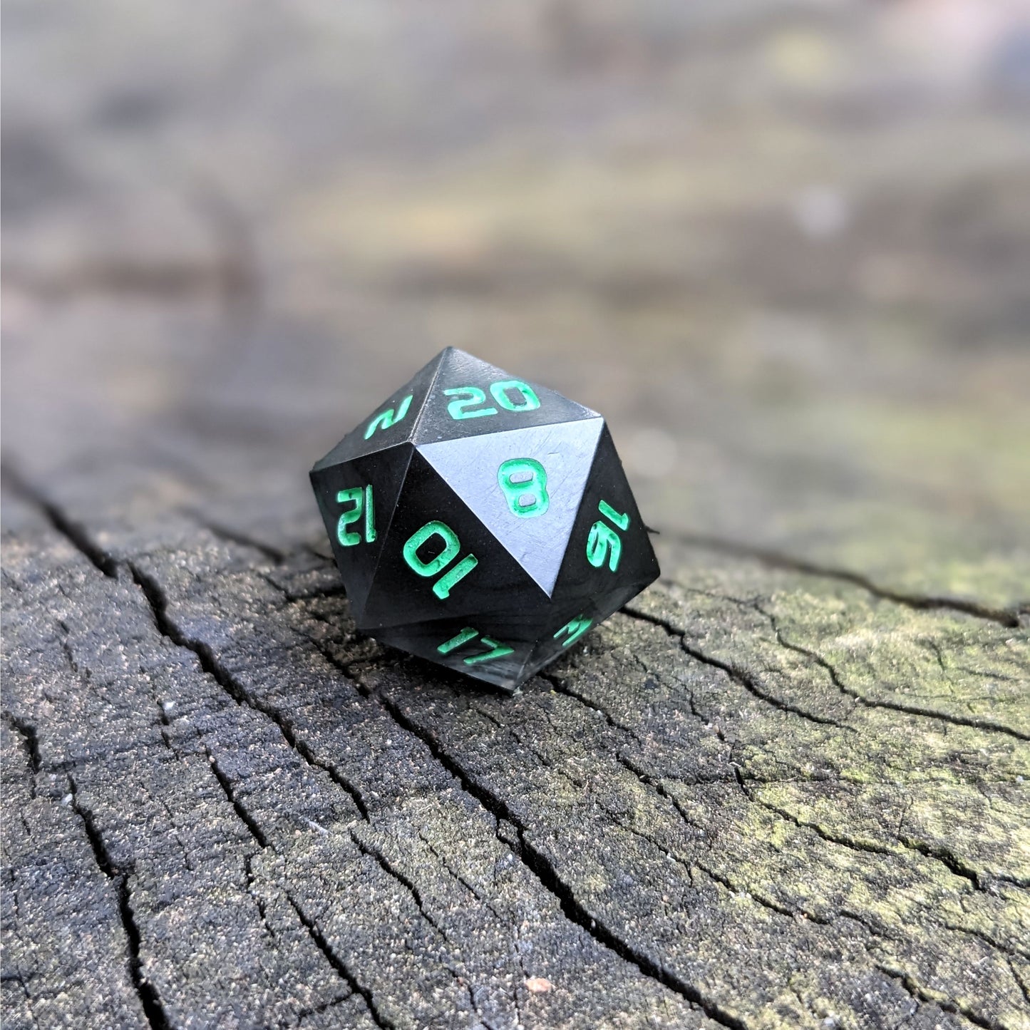A standard d20 with black swirls and green numbers sits on a wood stump with the 20 face up.