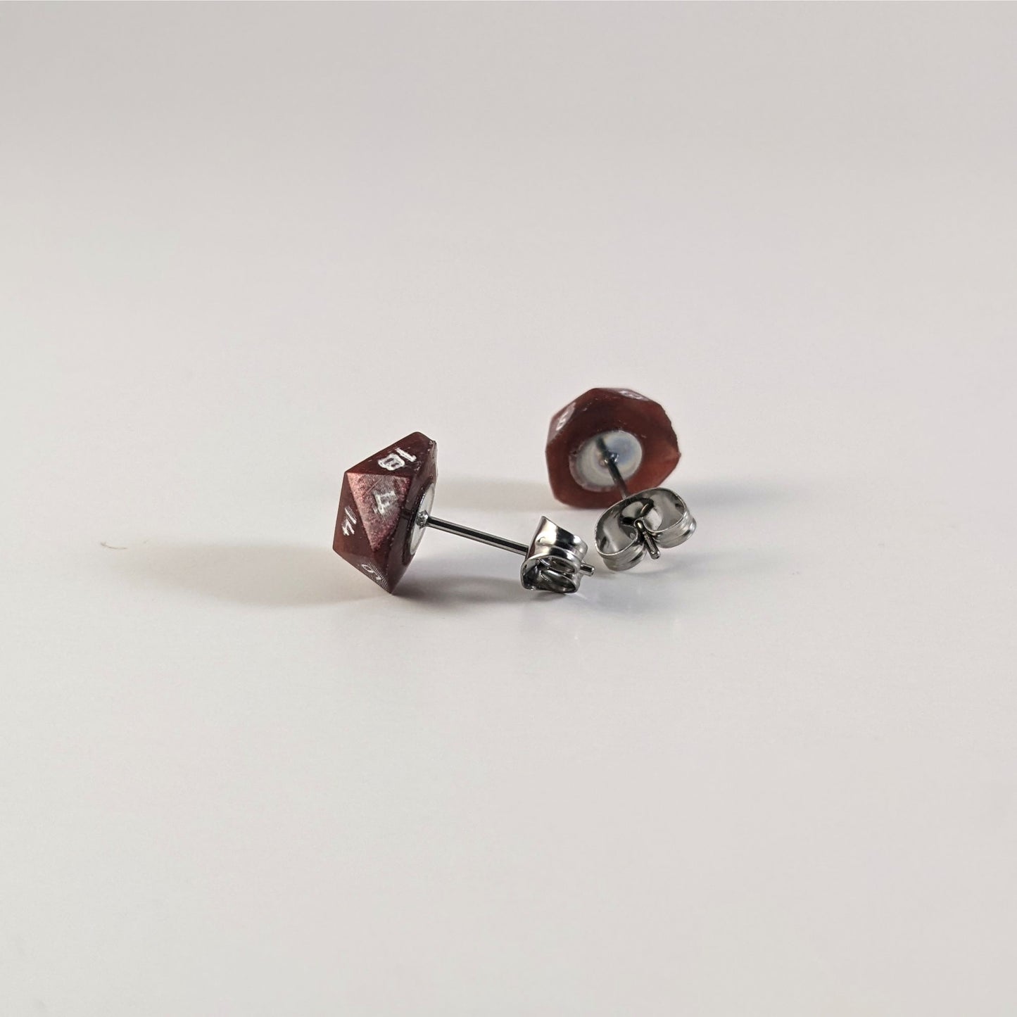 A single pair of handmade d20 earrings that are swirls of red with white numbers turned to show the metal alloy hardware and butterfly backs.