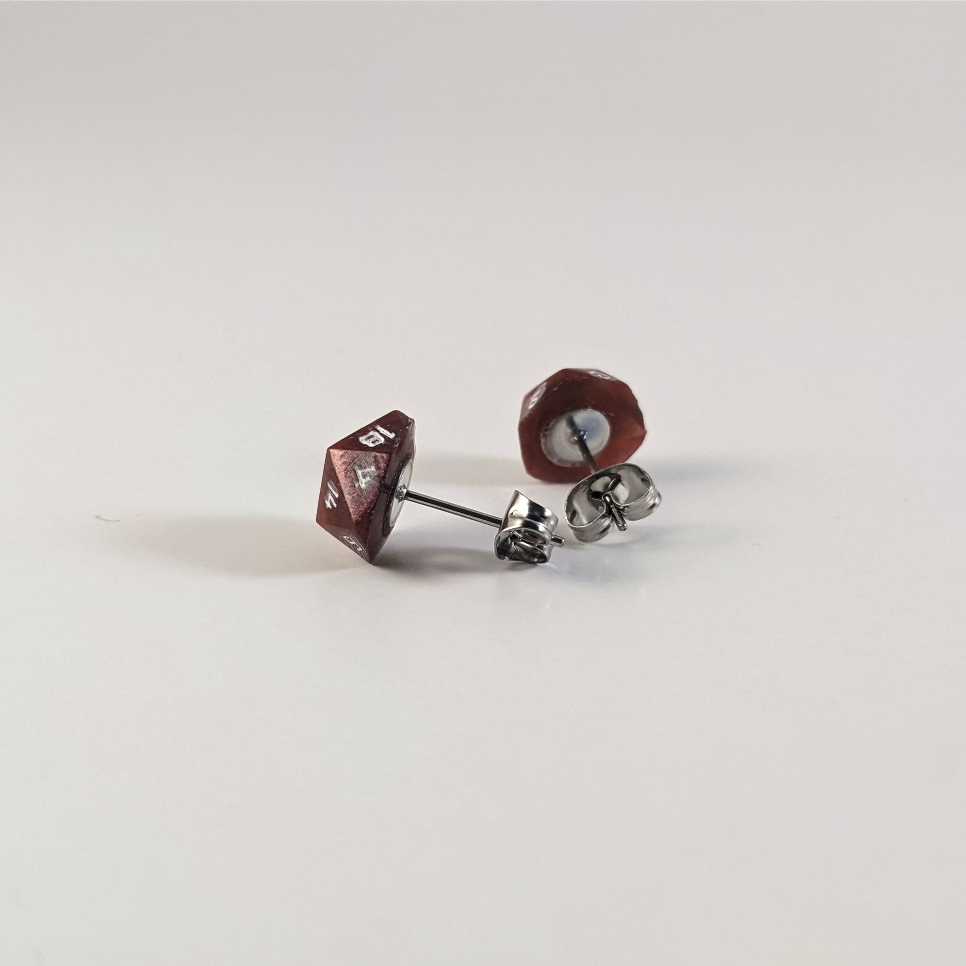 A single pair of handmade d20 earrings that are swirls of red with white numbers turned to show the metal alloy hardware and butterfly backs.