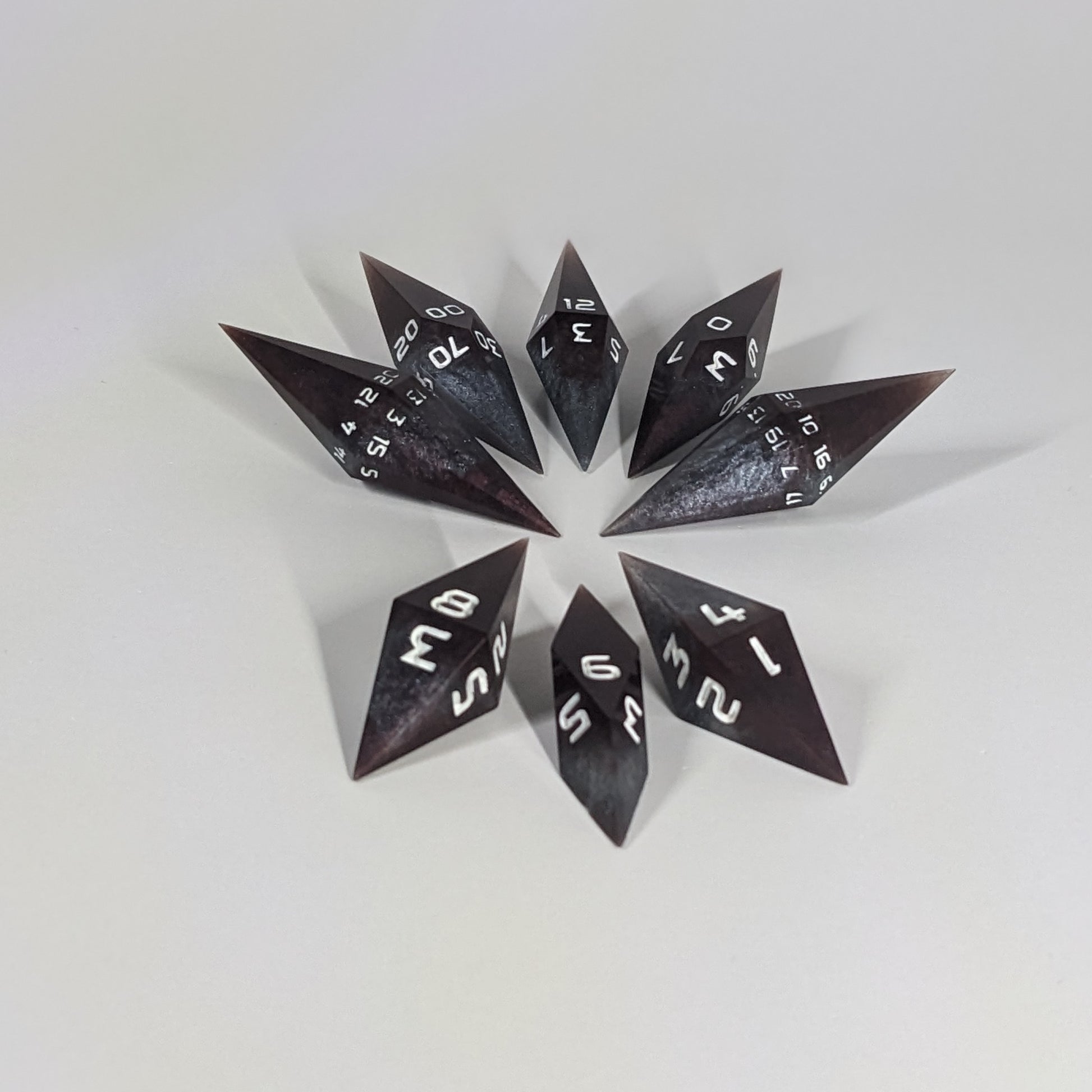 A complete set of resin dice featuring 2 d20s for advantage rolls. These deep maroon and dark silver with white numbers, slender handmade diamond dice are clustered in a tight circle on a white background, highlighting the quality of the artisan dice craftsmanship and the unique pointed shape.