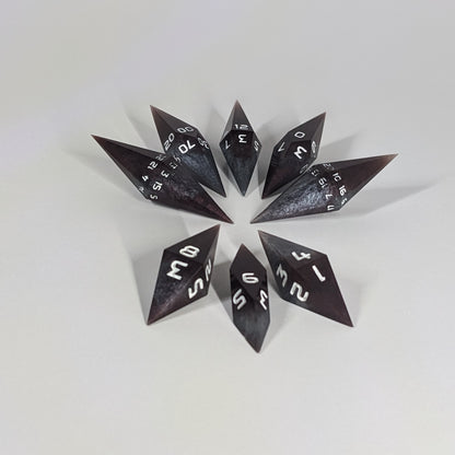 A complete set of resin dice featuring 2 d20s for advantage rolls. These deep maroon and dark silver with white numbers, slender handmade diamond dice are clustered in a tight circle on a white background, highlighting the quality of the artisan dice craftsmanship and the unique pointed shape.