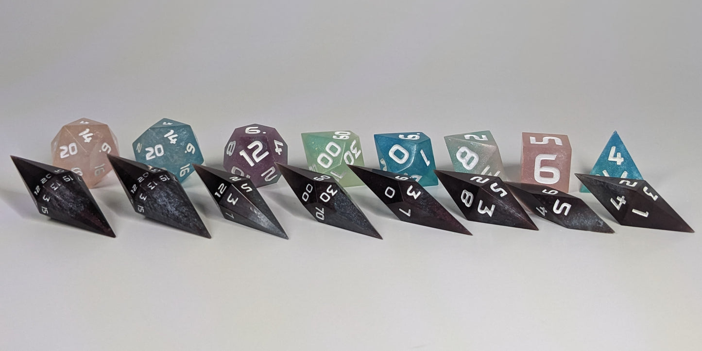 A size comparison of deep maroon and dark silver with white numbers, long pointed diamond handmade dice with standard shapes placed behind for scale. The photo emphasizes the length of the diamond dice being much greater than a standard set as well as the diamond set being much more slender. This artisan dice set features 2 d20s and rests on a seamless white background to highlight the elongated profile of the resin dice.