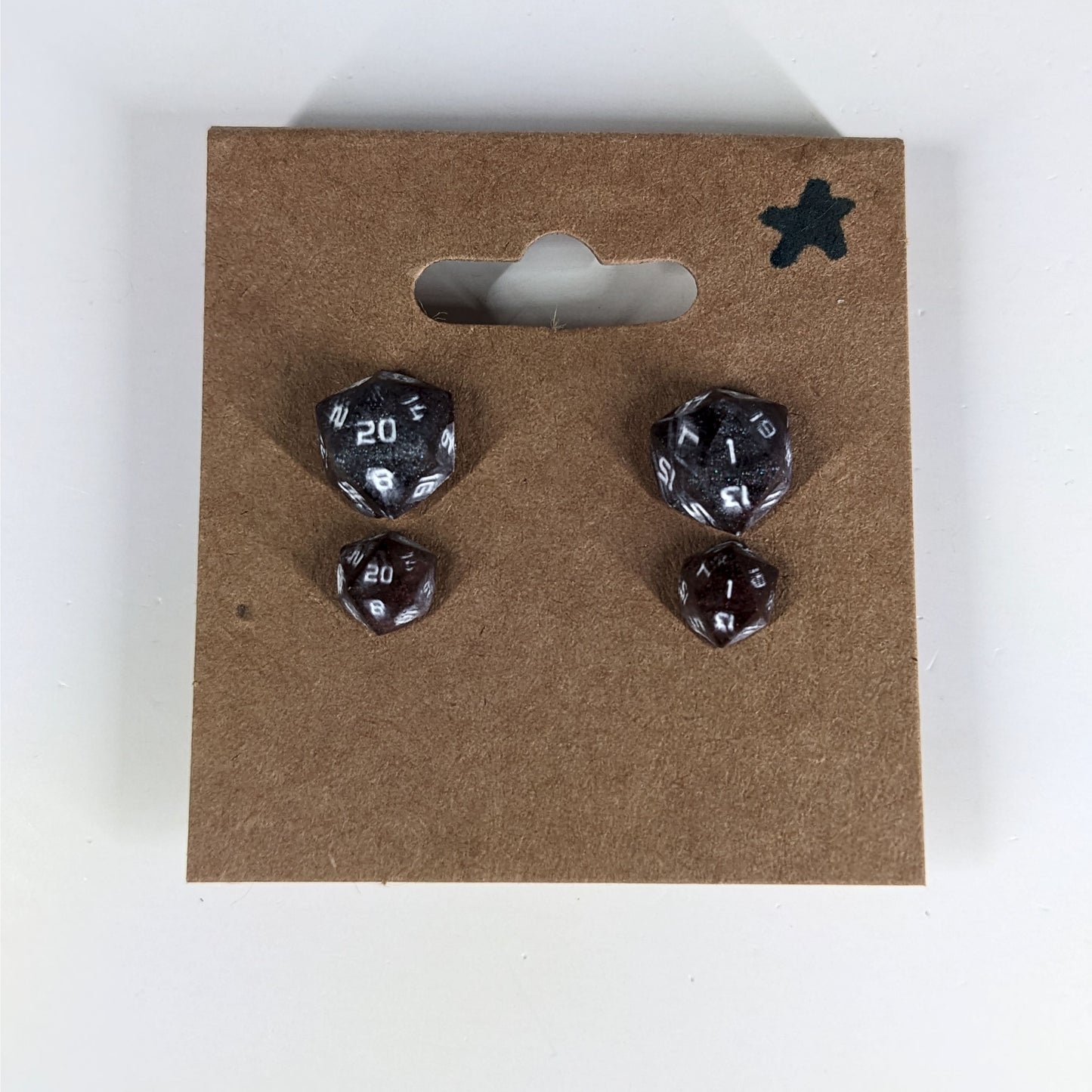 Two pairs of handmade d20 earrings with sterling silver hardware that are maroon and dark silver with white numbers on a kraft brown earring card with a star in the top right corner. The earrings on the left of each pair centers the 20 face and the earrings on the right of each pair centers the 1 face.