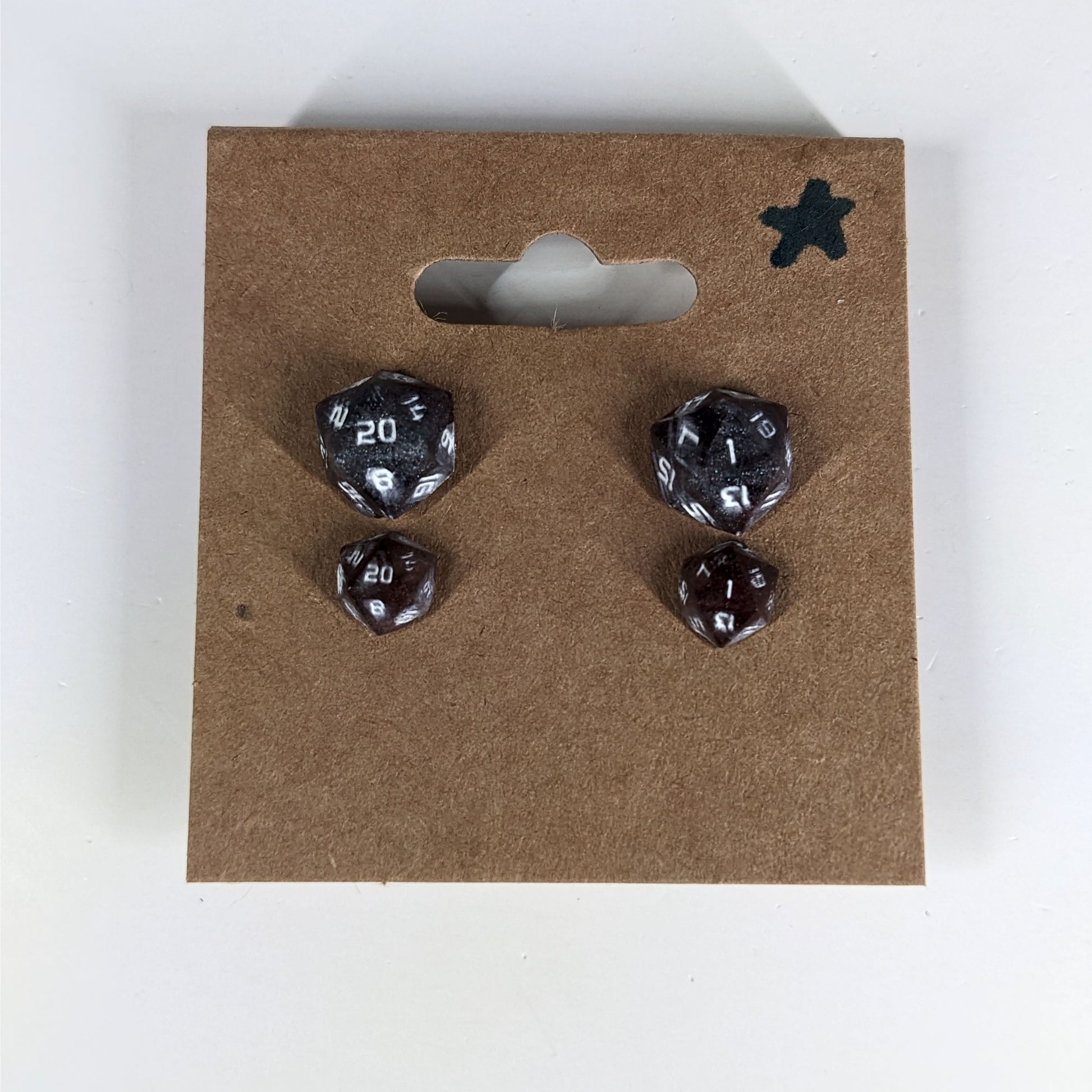 Two pairs of handmade d20 earrings with sterling silver hardware that are maroon and dark silver with white numbers on a kraft brown earring card with a star in the top right corner. The earrings on the left of each pair centers the 20 face and the earrings on the right of each pair centers the 1 face.
