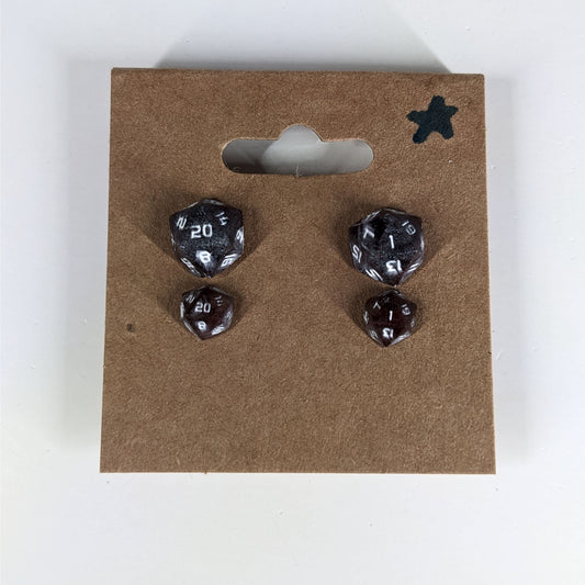 Two pairs of handmade d20 earrings with sterling silver hardware that are maroon and dark silver with white numbers on a kraft brown earring card with a star in the top right corner. The earrings on the left of each pair centers the 20 face and the earrings on the right of each pair centers the 1 face.