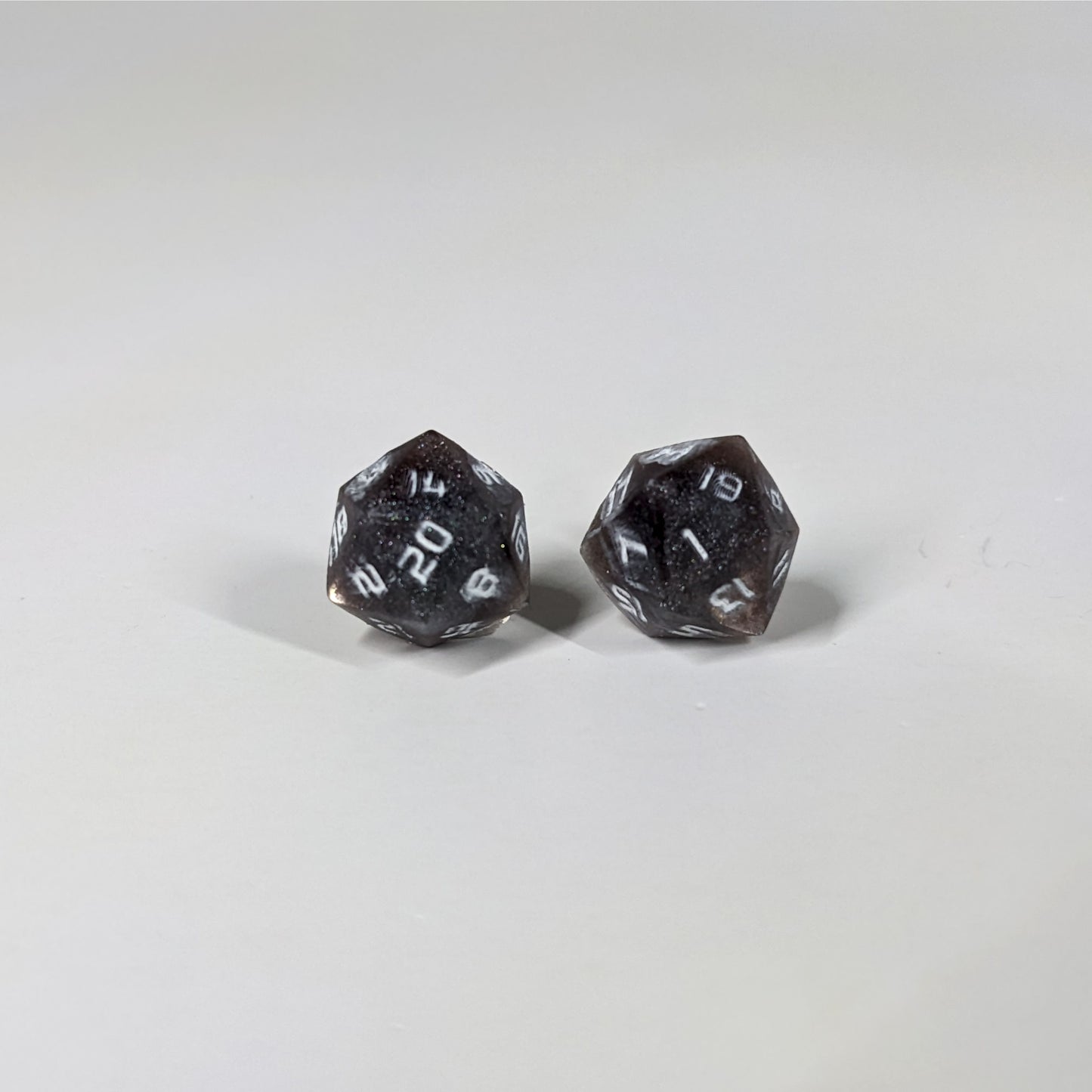A single pair of the larger size handmade d20 earrings with sterling silver hardware that are maroon and dark silver with white numbers on a white background. The earring on the left centers the 20 face and the earring on the right centers the 1 face.