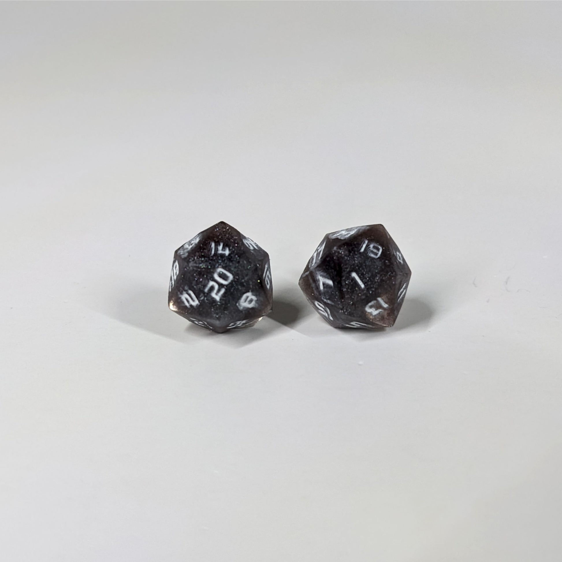 A single pair of the larger size handmade d20 earrings with sterling silver hardware that are maroon and dark silver with white numbers on a white background. The earring on the left centers the 20 face and the earring on the right centers the 1 face.