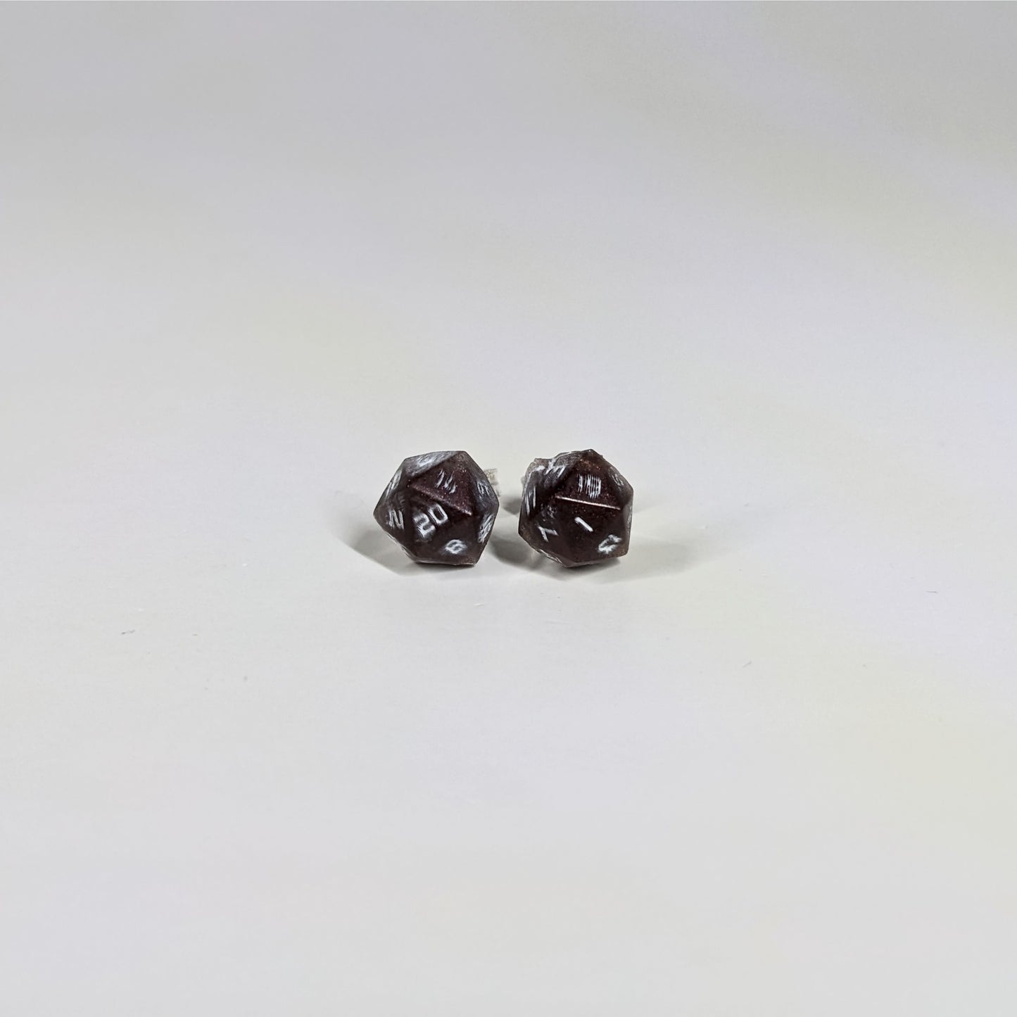 A single pair of the smaller size handmade d20 earrings with sterling silver hardware that are maroon and silver with white numbers on a white background. The earring on the left centers the 20 face and the earring on the right centers the 1 face.