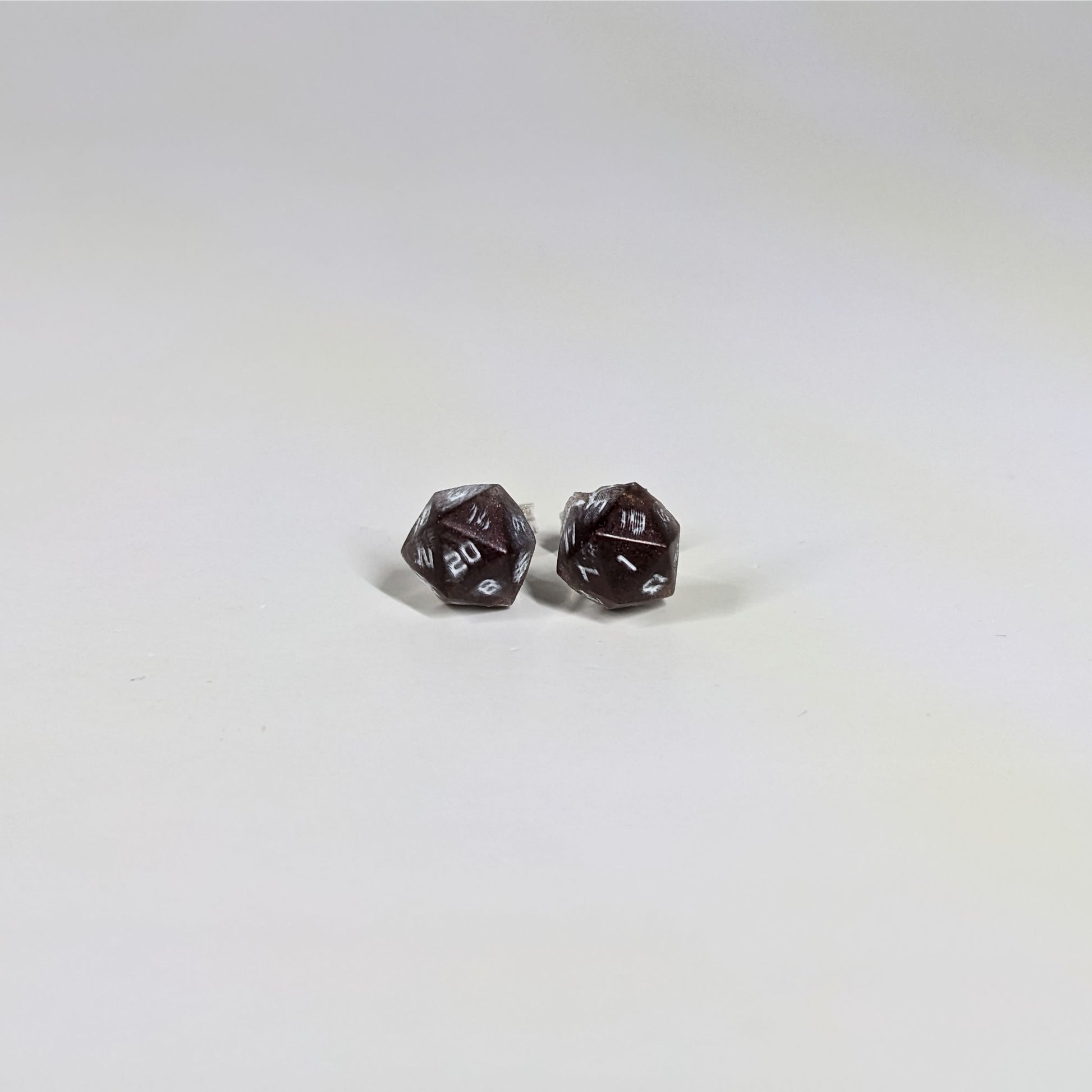 A single pair of the smaller size handmade d20 earrings with sterling silver hardware that are maroon and silver with white numbers on a white background. The earring on the left centers the 20 face and the earring on the right centers the 1 face.