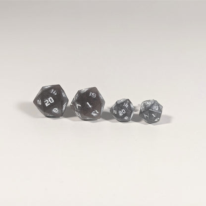 Two pairs of handmade d20 earrings with titanium hardware that are maroon and dark silver with white numbers on a white background sit in a line with the larger pair on the left and the smaller pair on the right. The earrings on the left of each pair centers the 20 face and the earrings on the right of each pair centers the 1 face.