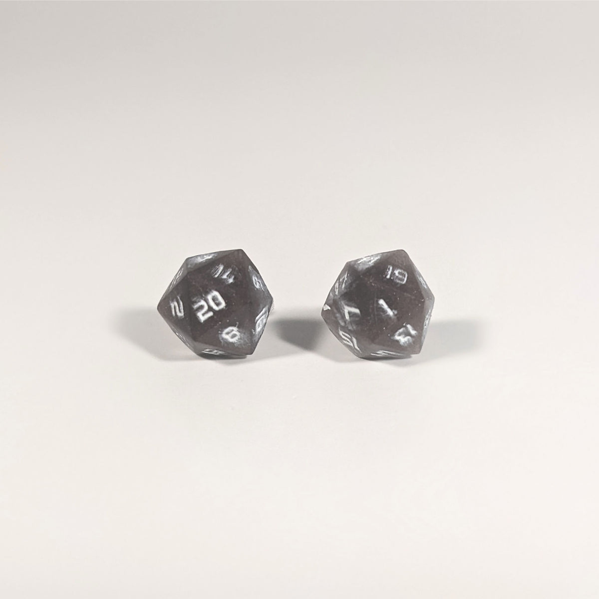 A single pair of the larger size handmade d20 earrings with titanium hardware that are maroon and dark silver with white numbers on a white background. The earring on the left centers the 20 face and the earring on the right centers the 1 face.