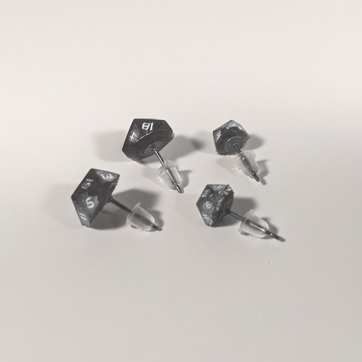 Two pairs of handmade d20 earrings that are maroon and dark silver with white numbers turned to show the titanium hardware and bell shaped rubber backs.