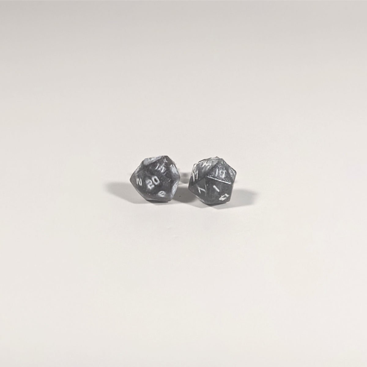 A single pair of the smaller size handmade d20 earrings with titanium hardware that are maroon and dark silver with white numbers on a white background. The earring on the left centers the 20 face and the earring on the right centers the 1 face.