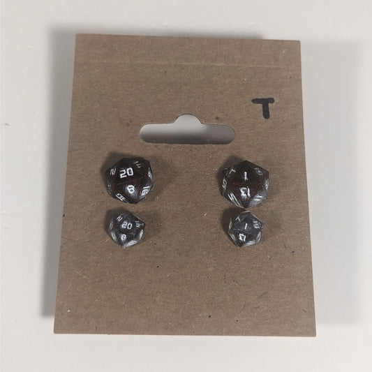 Two pairs of handmade d20 earrings with titanium hardware that are maroon and dark silver with white numbers on a kraft brown earring card with a T in the top right corner. The earrings on the left of each pair centers the 20 face and the earrings on the right of each pair centers the 1 face.