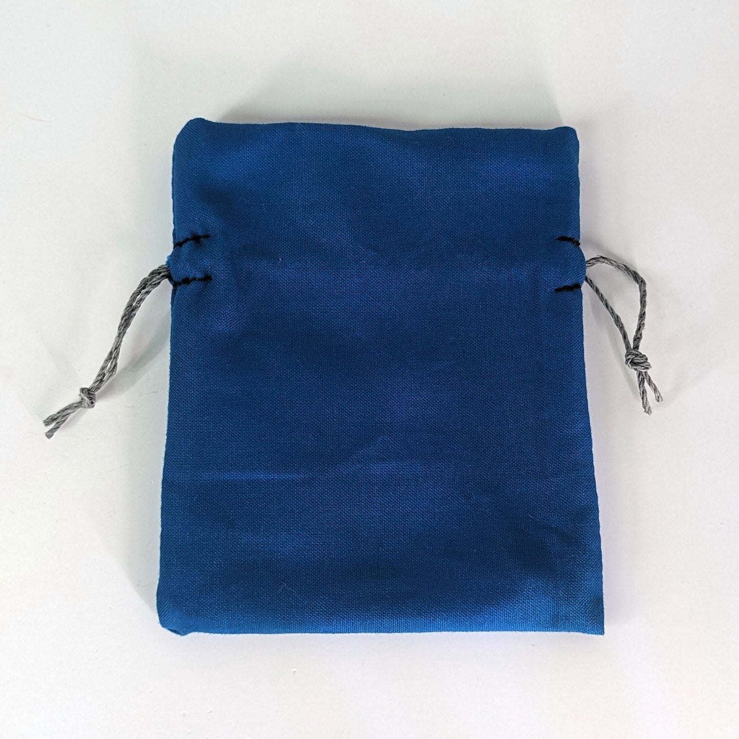 A small, handmade dice bag that is blue lays flat on a white background.