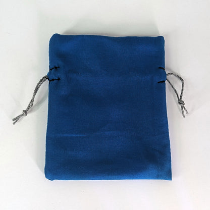 A small, handmade dice bag that is blue lays flat on a white background.