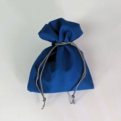 A small, handmade dice bag that is blue is tied closed on a white background.