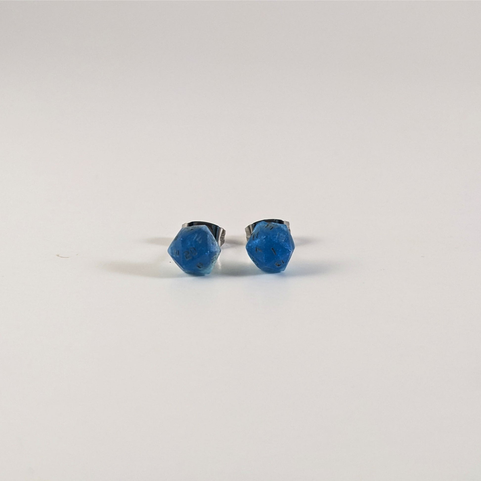 A single pair of the smaller size handmade d20 earrings that are swirls of blue with stormy gray numbers on a white background. The earring on the left centers the 20 face and the earring on the right centers the 1 face.