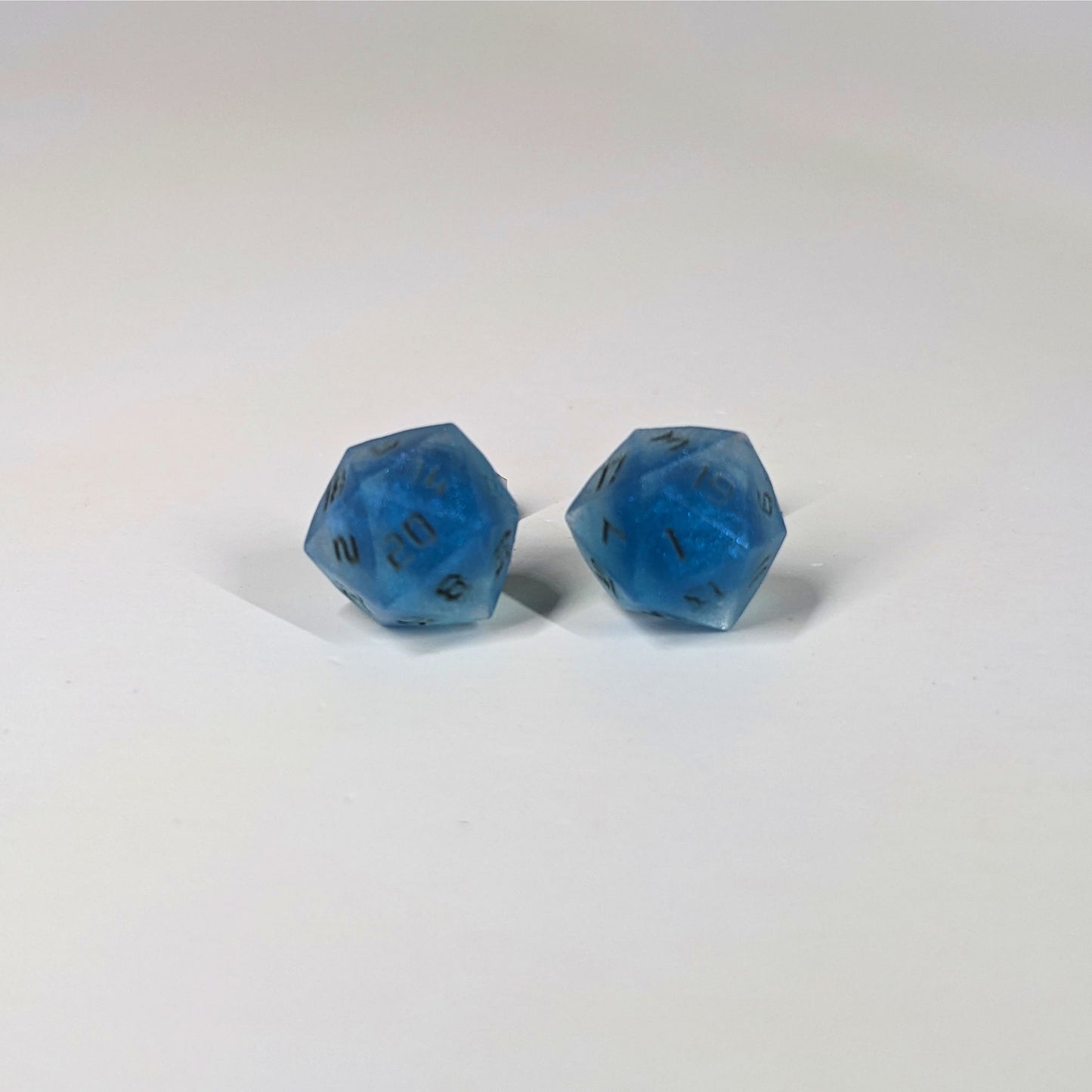 A single pair of the larger size handmade d20 earrings that are swirls of blue with stormy gray numbers on a white background. The earring on the left centers the 20 face and the earring on the right centers the 1 face.