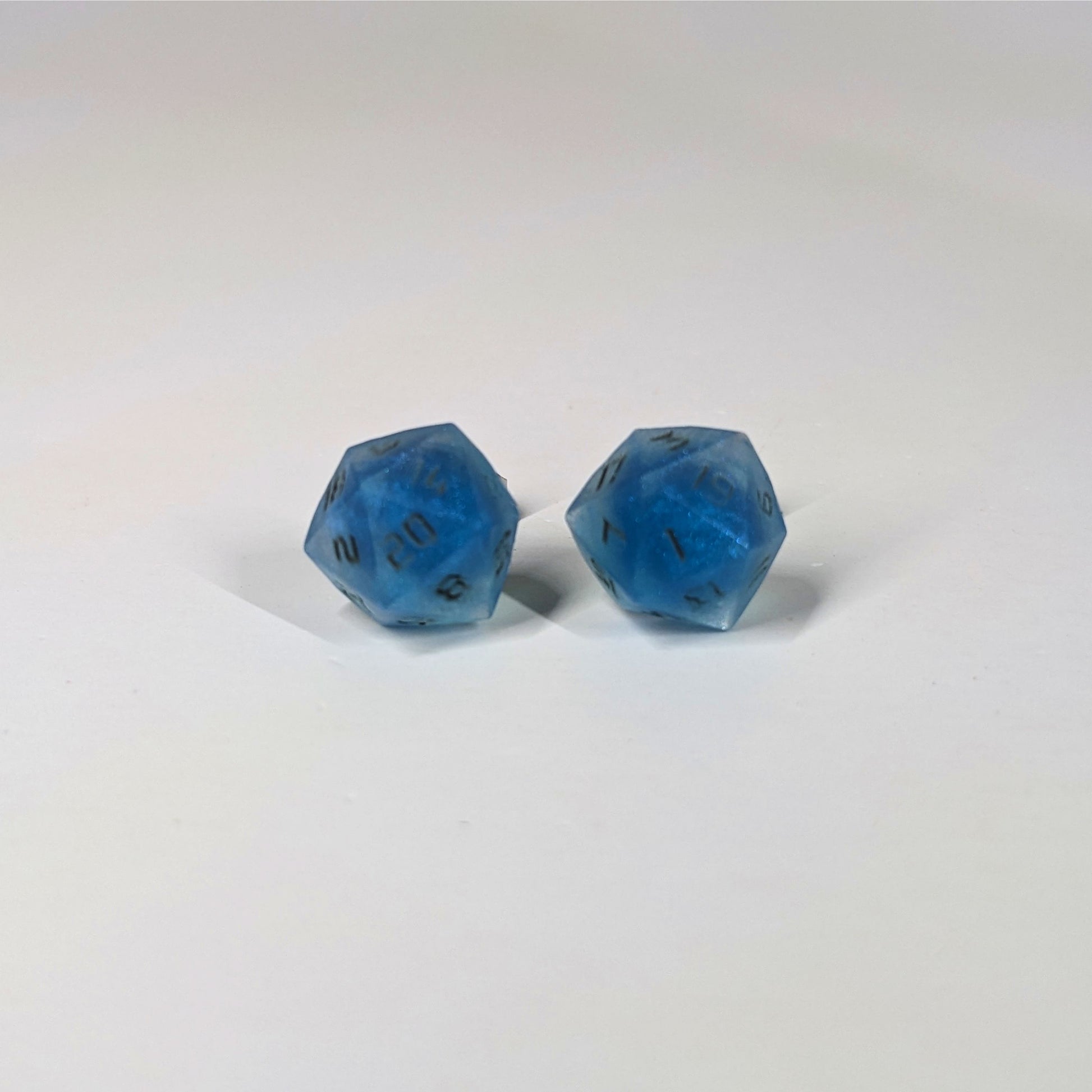 A single pair of the larger size handmade d20 earrings that are swirls of blue with stormy gray numbers on a white background. The earring on the left centers the 20 face and the earring on the right centers the 1 face.