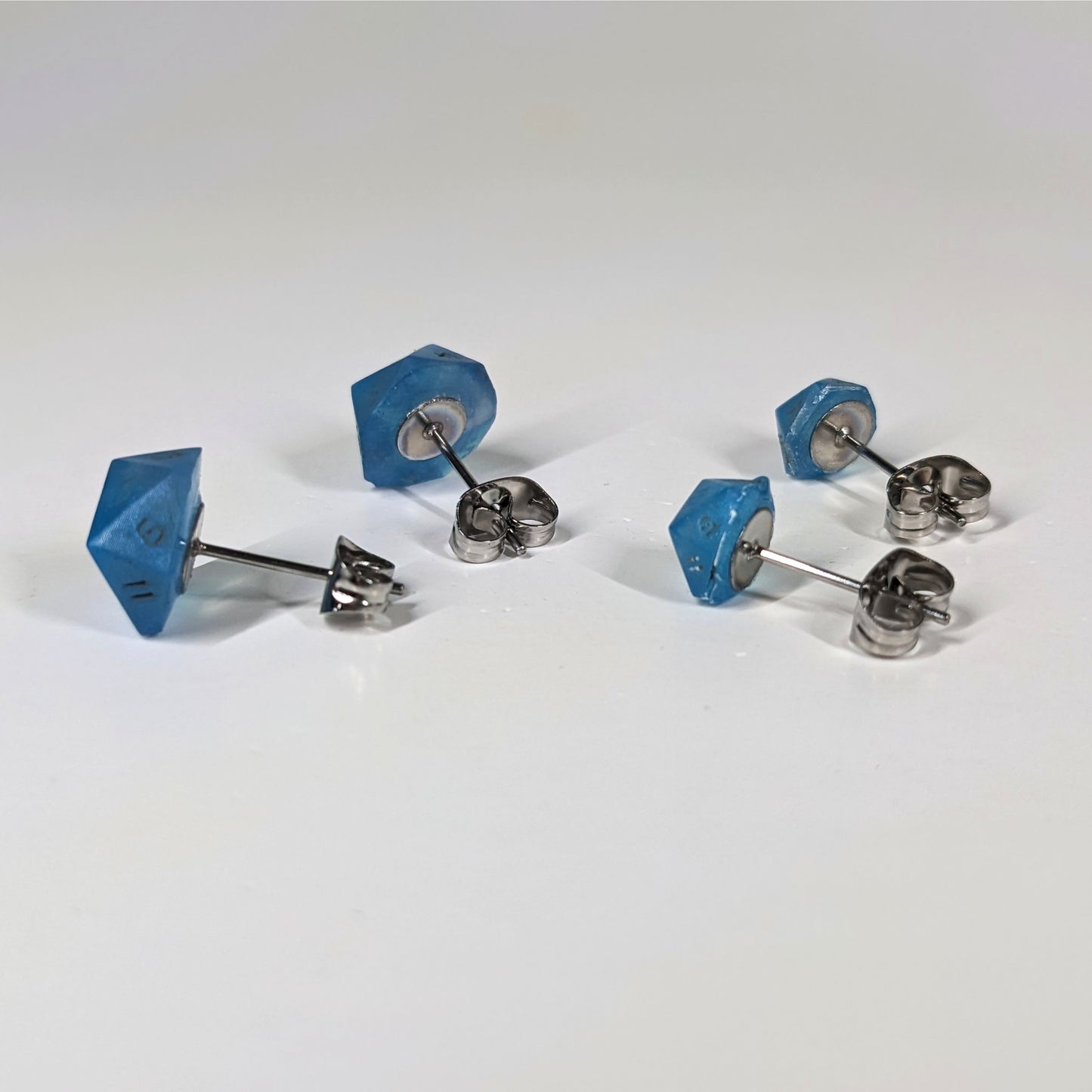 Two pairs of handmade d20 earrings that are swirls of blue with stormy gray numbers turned to show the metal alloy hardware and butterfly backs.