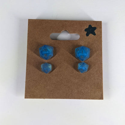 Two pairs of handmade d20 earrings with sterling silver hardware that are swirls of blue with stormy gray numbers on a kraft brown earring card with a star in the top right corner. The earrings on the left of each pair centers the 20 face and the earrings on the right of each pair centers the 1 face.