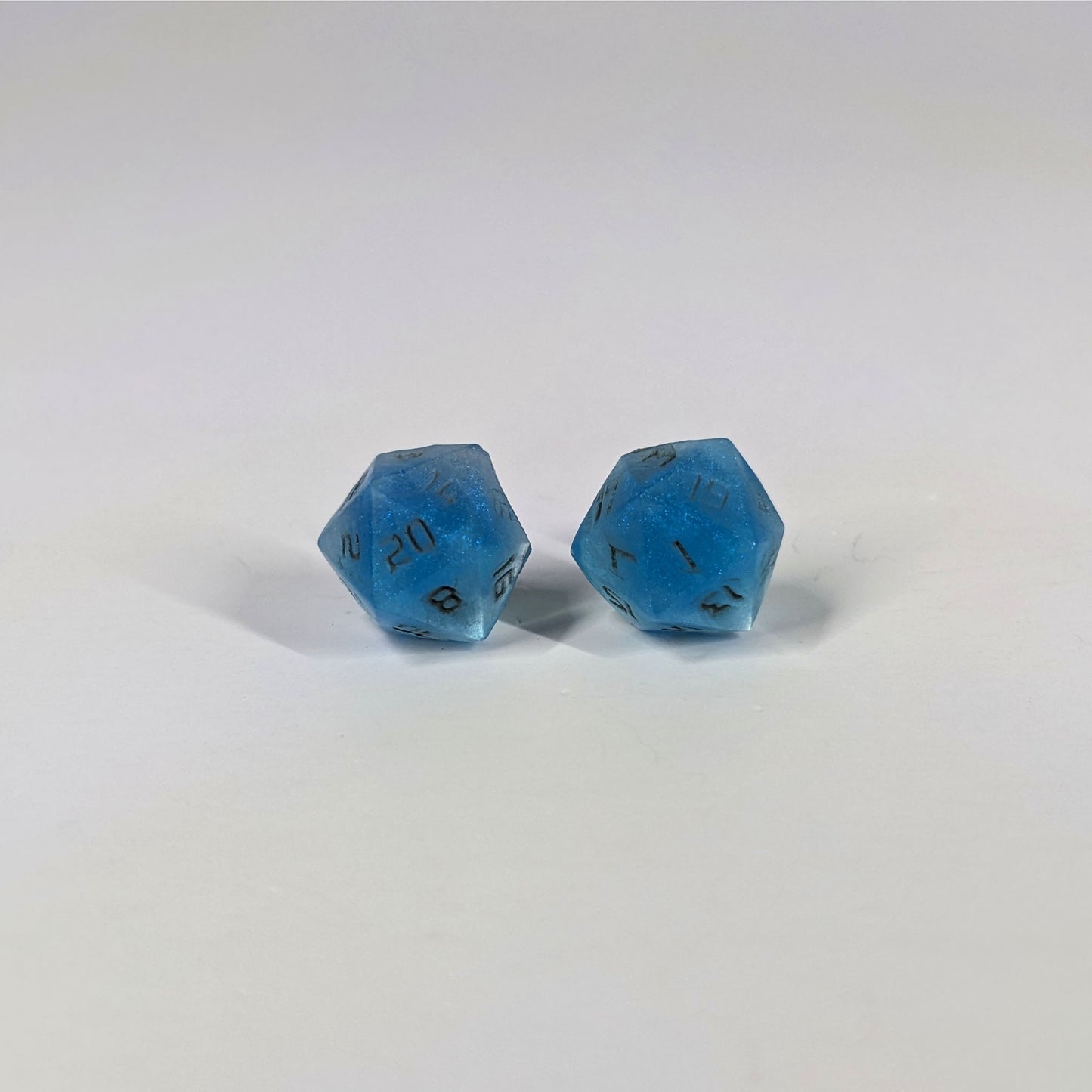 A single pair of the larger size handmade d20 earrings with sterling silver hardware that are swirls of blue with stormy gray numbers on a white background. The earring on the left centers the 20 face and the earring on the right centers the 1 face.