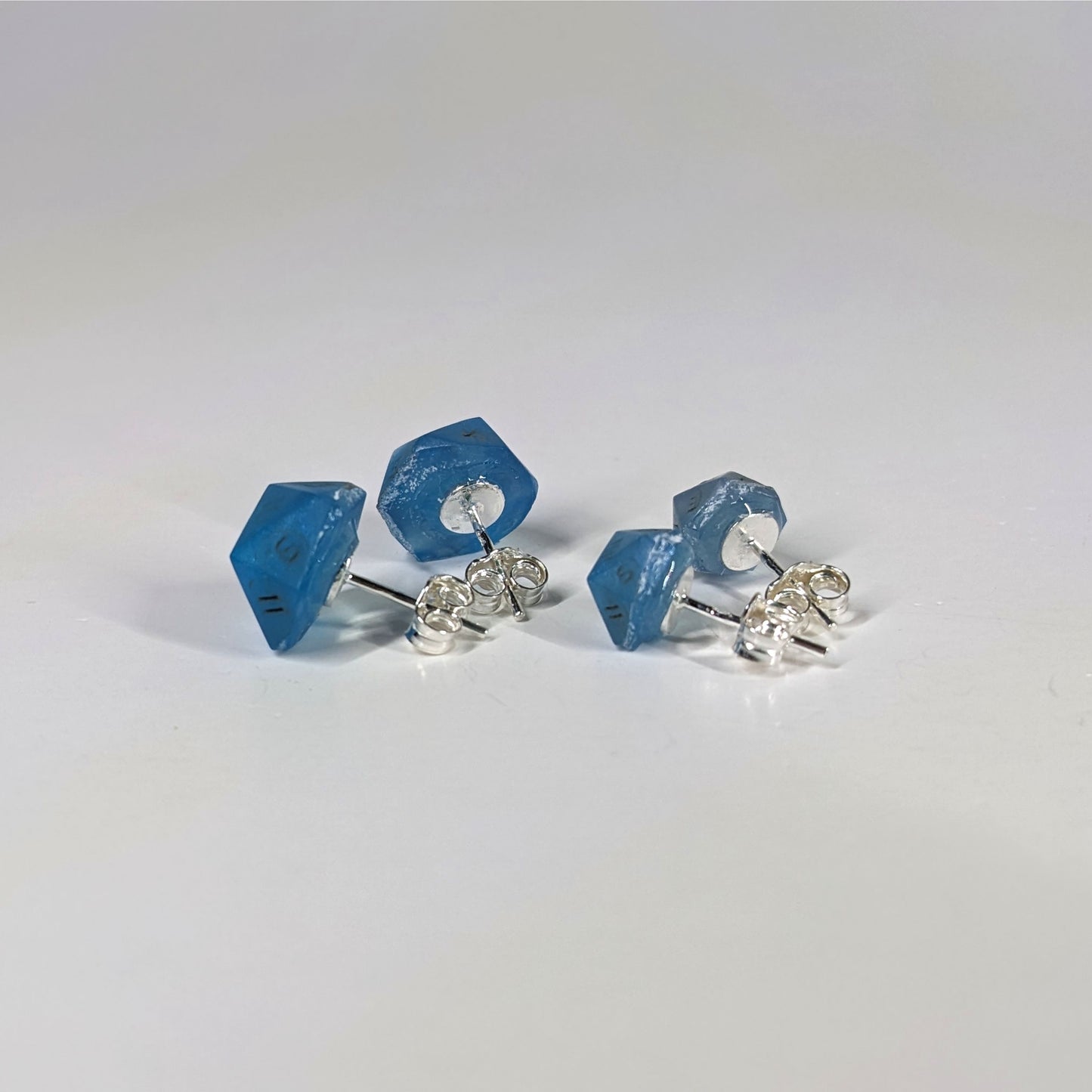 Two pairs of handmade d20 earrings that are swirls of blue with stormy gray numbers turned to show the sterling silver hardware and butterfly backs.