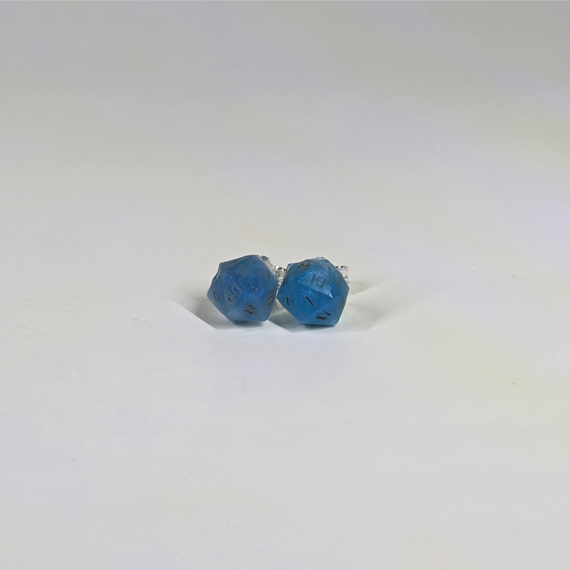 A single pair of the smaller size handmade d20 earrings with sterling silver hardware that are swirls of blue with stormy gray numbers on a white background. The earring on the left centers the 20 face and the earring on the right centers the 1 face.