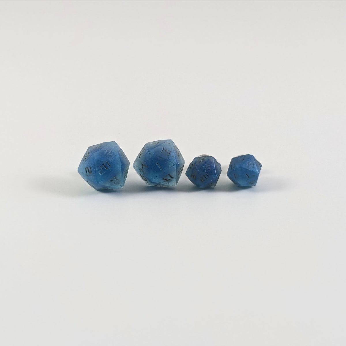 Two pairs of handmade d20 earrings with titanium hardware that are swirls of blue with stormy gray numbers on a white background sit in a line with the larger pair on the left and the smaller pair on the right. The earrings on the left of each pair centers the 20 face and the earrings on the right of each pair centers the 1 face.