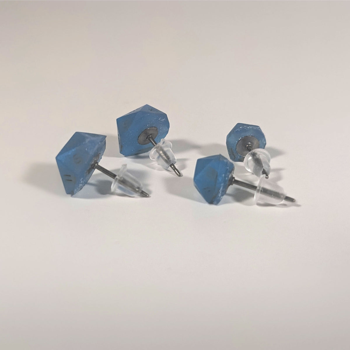 Two pairs of handmade d20 earrings that are swirls of blue with stormy gray numbers turned to show the titanium hardware and bell shaped rubber backs.