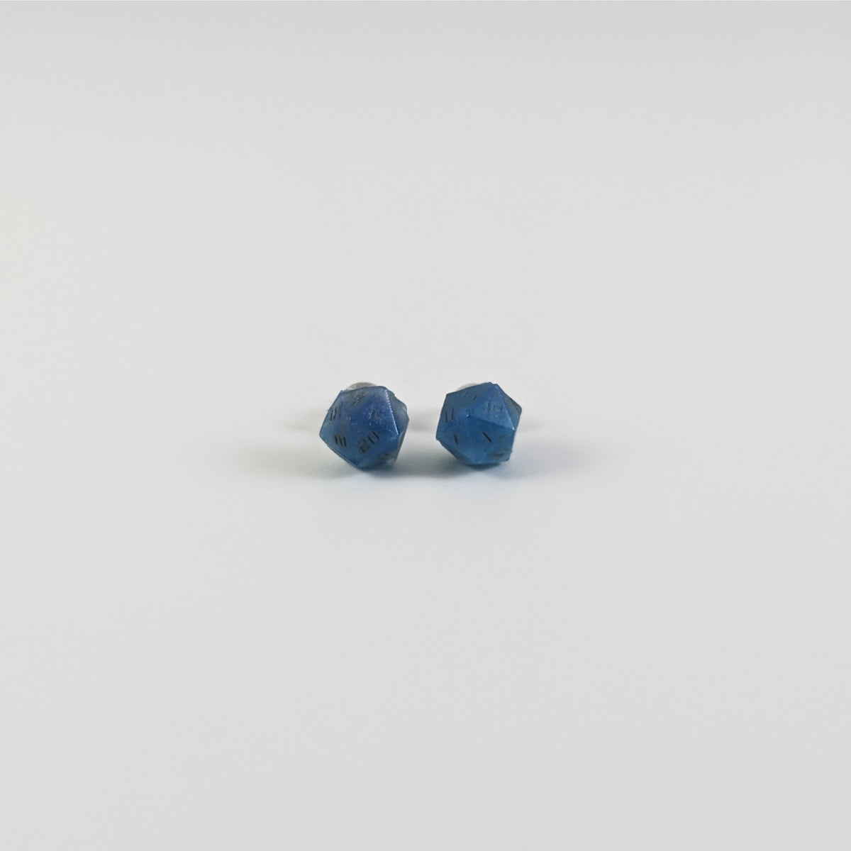 A single pair of the smaller size handmade d20 earrings with titanium hardware that are swirls of blue with stormy gray numbers on a white background. The earring on the left centers the 20 face and the earring on the right centers the 1 face.