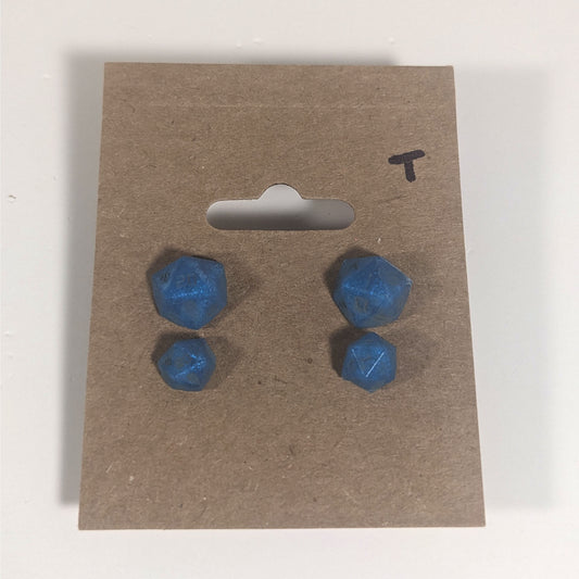 Two pairs of handmade d20 earrings with titanium hardware that are swirls of blue with stormy gray numbers on a kraft brown earring card with a T in the top right corner. The earrings on the left of each pair centers the 20 face and the earrings on the right of each pair centers the 1 face.