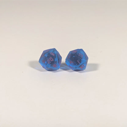 A single pair of the larger size handmade d20 earrings with titanium hardware that are rich blue with bright pink numbers on a white background. The earring on the left centers the 20 face and the earring on the right centers the 1 face.