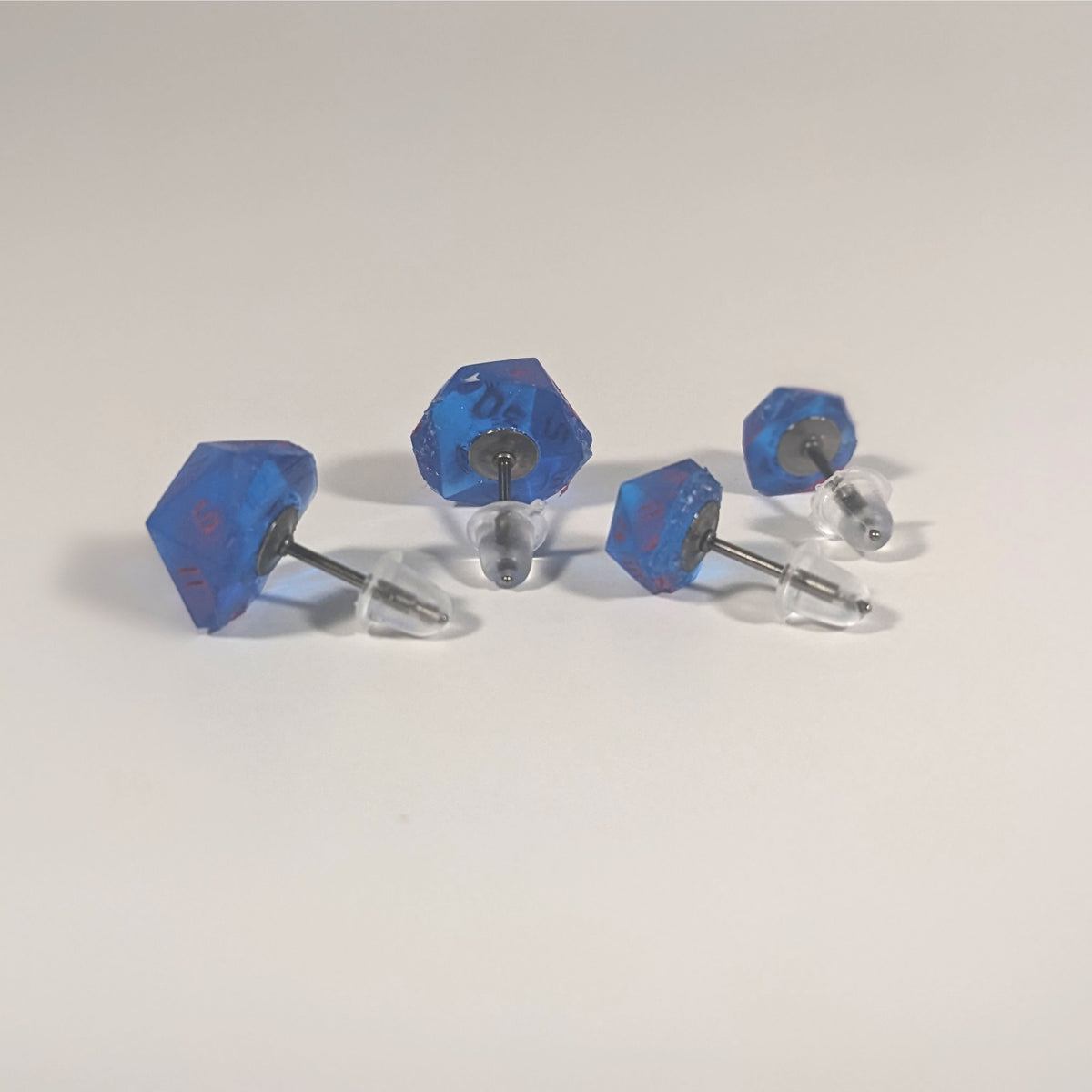 Two pairs of handmade d20 earrings that are rich blue with bright pink numbers turned to show the titanium hardware and bell shaped rubber backs.