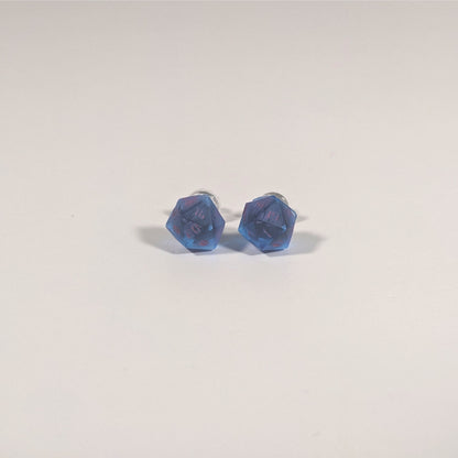 A single pair of the smaller size handmade d20 earrings with titanium hardware that are rich blue with bright pink numbers on a white background. The earring on the left centers the 20 face and the earring on the right centers the 1 face.