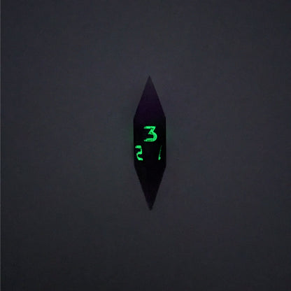 A high angle view of a diamond d3 with swirls of purple and green with black numbers that glow in the dark on a white background. This photo is taken in the dark to show the black numbers glowing green in the dark.