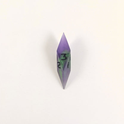 A high angle view of a diamond d3 with swirls of purple and green with black numbers that glow in the dark on a white background.