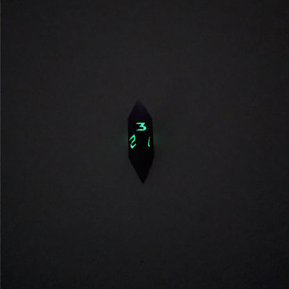 A mid angle view of a diamond d3 with swirls of purple and green with black numbers that glow in the dark on a white background. This photo was taken in the dark to show the black numbers glowing green in the dark.