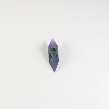 A mid angle view of a diamond d3 with swirls of purple and green with black numbers that glow in the dark on a white background.