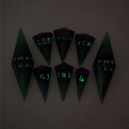 A dagger style DnD dice set that is  green and purple with black numbers that glow in the dark is arranged with a d20 each on the right and left, with the d%, d12, and d10 along the top and the d6, d8, and d4 along the bottom, all in line with the d20s. The photo was taken in the dark to show the black numbers glowing green.