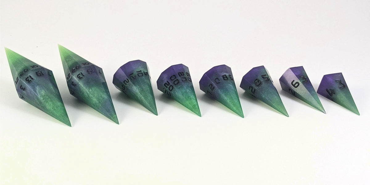 A straight on photo of a complete set of dagger DnD dice that are green and purple with black numbers that glow in the dark arranged in a straight line with points angled toward the right. They are lined up with the 2 d20s on the left going down to the d4 on the right side. The highest value number of each die is facing forward.