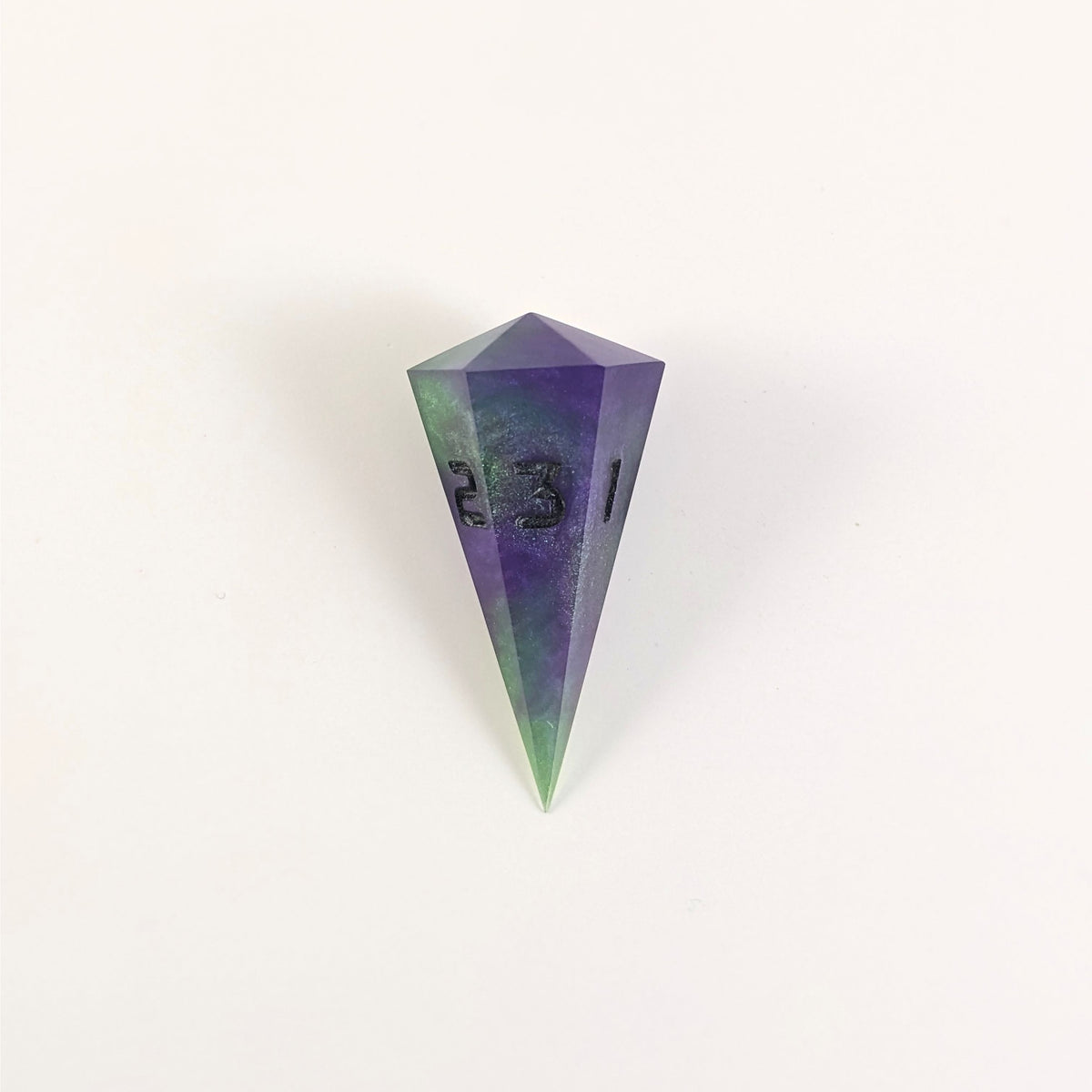 A high angle view of a dagger d3 with swirls of purple and green with black numbers that glow in the dark on a white background.