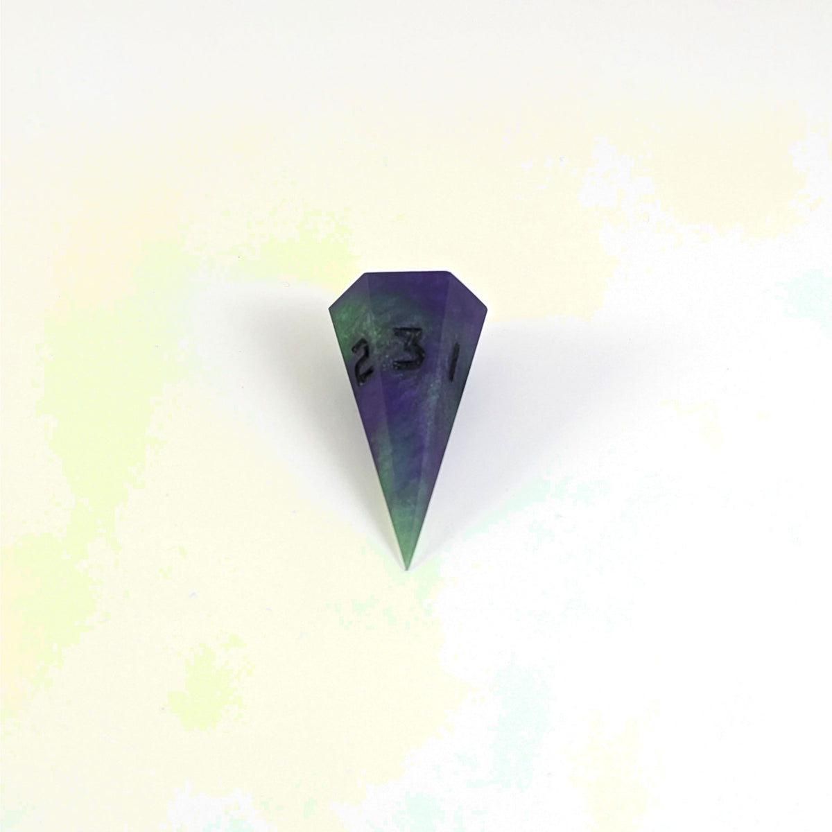 A mid angle view of a dagger d3 with swirls of purple and green with black numbers that glow in the dark on a white background.