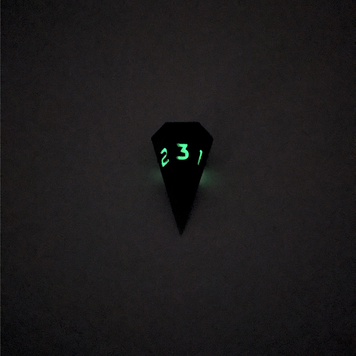A mid angle view of a dagger d3 with swirls of purple and green with black numbers that glow in the dark on a white background. This photo was taken in the dark to show the black numbers glowing green in the dark.