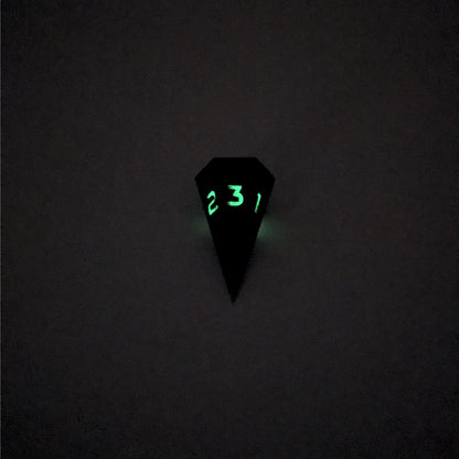 A mid angle view of a dagger d3 with swirls of purple and green with black numbers that glow in the dark on a white background. This photo was taken in the dark to show the black numbers glowing green in the dark.