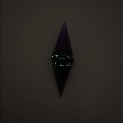 A high angle view of a diamond d20 with swirls of purple and green with black numbers that glow in the dark on a white background. This photo is taken in the dark to show the black numbers glowing green in the dark.